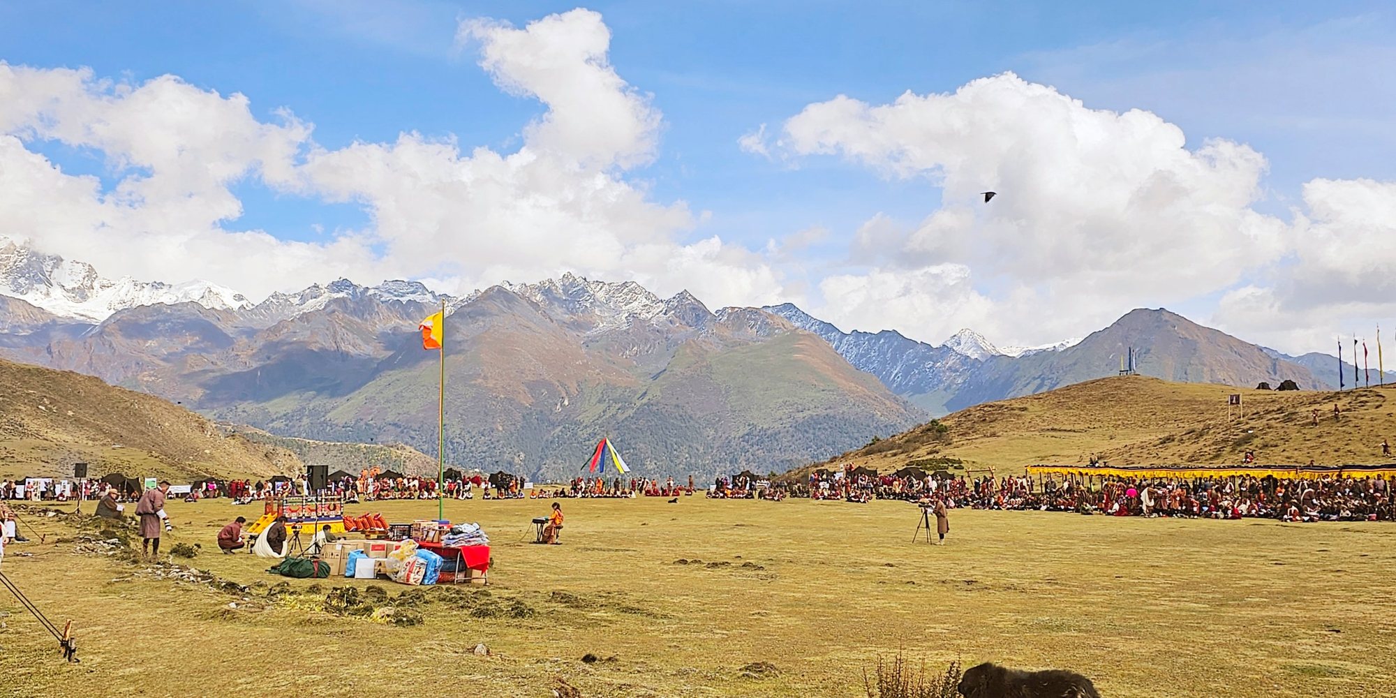 A high grassy field ringed by snow-capped mountains, with the festival crowd seated along the far edge and a lone keyboard set up in the middle.